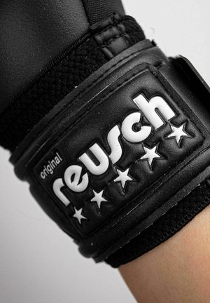 Schwarzer Reusch Sporthandschuh-Handgelenksriemen mit weiß geprägt Markennamen und fünf Sternen auf einem erhöhten rechteckigen Patch.