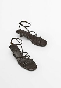 Musta nauhakiilakorko sandaalit, joissa on palmikko ankle strap ja neliömäinen kärki, valkoisella taustalla.
