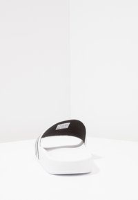 Black and white slide sandal with a textured black strap and a white platform sole, featuring a flat design suitable for casual wear.