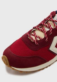 Baskets rouges foncées avec une tige en mesh agrémentée d'accents en daim, logo blanc, semelle extérieure épaisse beige et lacets contrastants blancs et rouges.