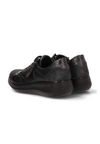 Zapatillas de cuero negras de caña baja con cremalleras laterales y suelas de goma gruesas, vistas desde atrás y ligeramente en ángulo hacia un lado.