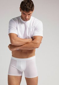 Camiseta de algodón blanco de cuello redondo combinada con bóxers blancos. La tela es suave, con un diseño ajustado y una cinturilla elástica.
