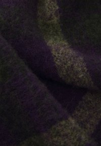 Gyapjú anyag sötétlila és olívazöld színben, puha, bolyhos textúrával, változatos mintázattal, amely egyes részek sima, míg mások texturáltak.