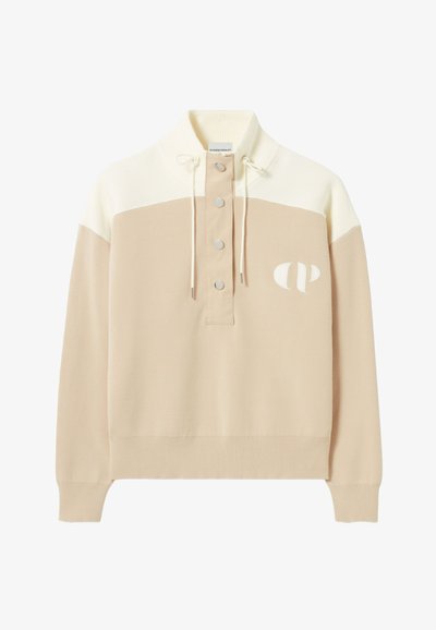 Pull beige et crème avec un col haut, un design côtelé, quatre boutons au cou et un logo sur la poitrine. Texture douce et coupe décontractée.