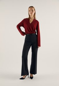 Bluză roșie cu mâneci lungi și decolteu în V; asortată cu pantaloni negri croiți și pantofi negri cu vârf ascuțit, creând o siluetă elegantă.