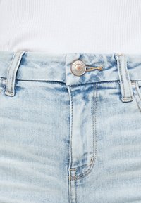 Ljusblå denimjeans med en blekt finish, med en silverknappstängning och kontrasterande sömmar längs midjebandet och fickorna.