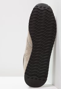 Semišové tenisky s texturovaným světle šedým svrškem, černou gumovou podrážkou s vlnkovým vzorem a embosovaným logem.