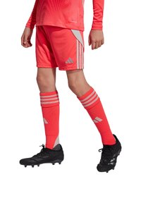 Helle korallenfarbene Sportuniform mit einem Langarmshirt, Shorts mit silbernen Akzenten und passenden knielangen Socken, kombiniert mit schwarzen Fußballschuhen.