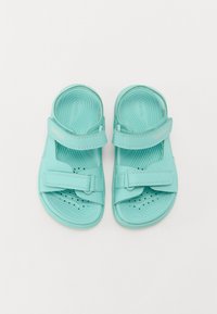 Sandálias turquesa com sola texturizada, tiras ajustáveis e perfurações para respirabilidade, apresentando o logótipo "GEOX" na tira.