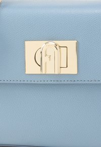 Hele sinine nahast käekott tekstuurse viimistlusega ja kuldtrooniga kinnitus, millel on stiliseeritud täht "F". Õmblused servade ümber.