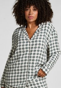 Koszula piżamowa zapinana na guziki, wykonana z miękkiego materiału, w zielono-białą kratkę z małymi serduszkami. Długie rękawy i luźny krój.