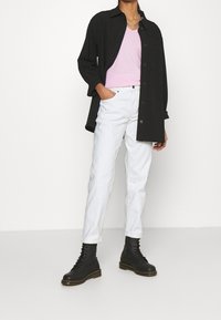 Camicia nera a maniche lunghe sopra un top rosa a scollo a V, abbinata a jeans bianchi e stivali neri stringati. Design semplice con colori a contrasto.