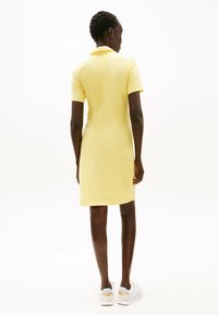 Gelbes Polo-Kleid mit kurzen Ärmeln, glatte Baumwolltextur, Kragen-Detail, knielang, kombiniert mit weißen Sneakers.