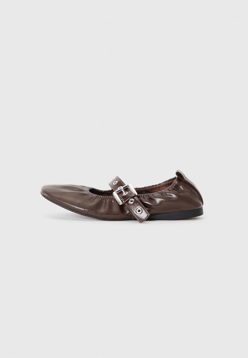 Ballerine plate en cuir marron avec des bords élastiqués et une bride à boucle argentée sur le dessus, vue de profil sur fond blanc.
