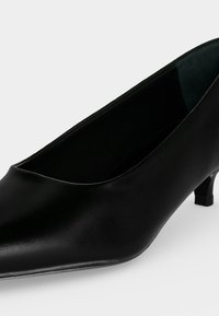 Escarpin femme en cuir noir à petit talon, bout pointu et petit talon kitten sur fond clair.