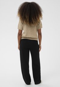 Beige rövid ujjú kötött pulóver fekete, bő szárú nadrággal párosítva. A pulóver puha tapintású, míg a nadrág hátoldalán zsebek találhatóak.