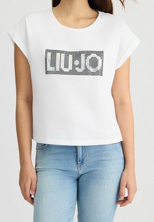 Vrouw draagt een wit cropped top met korte mouwen met een gepixeld 'LIU·JO' logo en lichtblauwe high-waisted jeans.