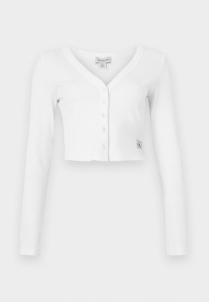Weißer, taillierter Cardigan mit V-Ausschnitt, langen Ärmeln und sechs Knöpfen auf der Vorderseite. Besitzt ein kleines Markenetikett am unteren linken Rand.
