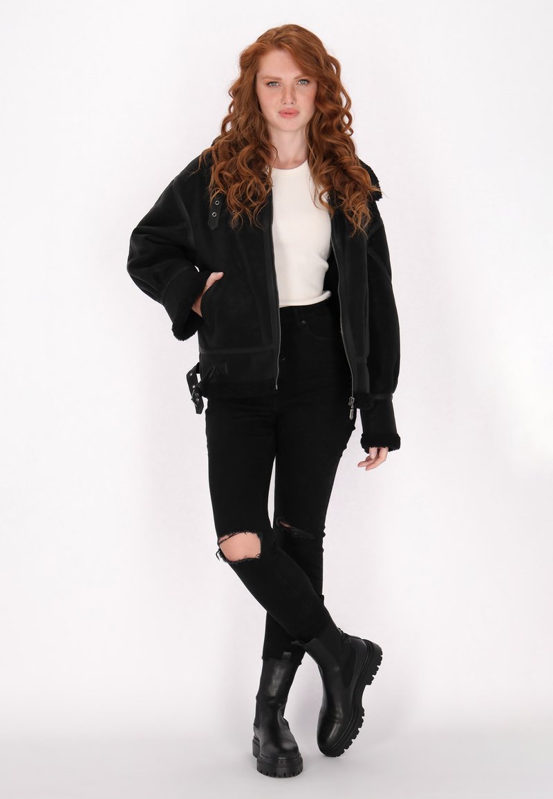 Schwarze, oversized Jacke mit plüschigem Innenfutter, großen Taschen, Reißverschluss und Knopfakzenten. Kombiniert mit schwarzen, zerfetzten Skinny-Jeans und klobigen Stiefeln.