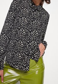 Black button-up shirt with white speckled pattern, paired with shiny green pants. Features a collar and long sleeves.