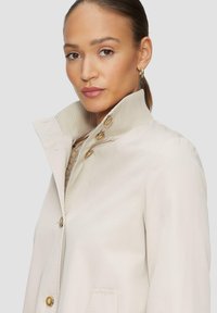 Beige trenchcoat met een gestructureerde geribde kraag, frontknopen en zijzakken. De stof lijkt glad met een goed passend ontwerp.