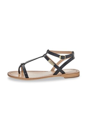 Black leather sandal with cross straps, textured surface, and a low wooden heel. Features a buckle closure and a natural footbed.