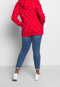 Czerwona bluza z kapturem, ozdobiona wielokolorowym wzorem kwiatowym. Do tego jasnoniebieskie, podwinięte rurki i białe tenisówki.