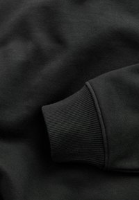 Tejido de sudadera negro con puños de canalé. La textura parece suave y lisa, con un diseño simple y sin adornos, sin patrones ni herrajes.