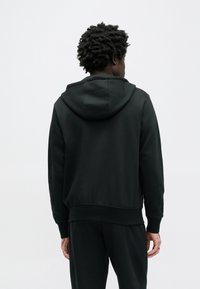 Čierna mikina s kapucňou z mäkkej látky. Má voľný strih, rebrované manžety a jednoduchý dizajn bez viditeľných log alebo vzorov.