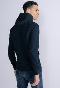 Marineblauwe hooded sweatshirt met een zachte textuur, met lange mouwen en een gebogen zoom, gecombineerd met denim jeans. Achteraanzicht weergegeven.