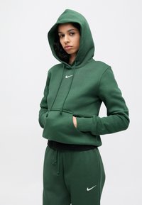 Sweatshirt verde cropped com capuz ajustável, bolso frontal e logótipo branco da Nike. Confeccionado em tecido macio com punhos e bainha canelados.