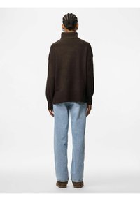 Maglione oversize marrone con dolcevita e orlo a costine, abbinato a jeans blue chiaro a gamba dritta e stivaletti marroni.