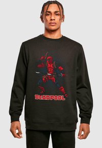 Fekete pulóver, amelyen egy piros Deadpool grafika l�átható, képregény-stílusú dizájnnal, hangsúlyos vonalakkal és dinamikus pózzal.