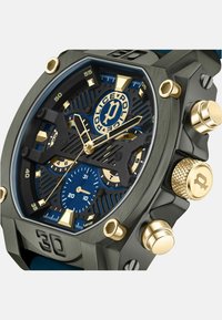 Orologio in metallo grigio con quadrante blu, accenti dorati e dettagli neri testurizzati. Presenta grandi sottoquadranti e numeri in grassetto. Design della corona esagonale.
