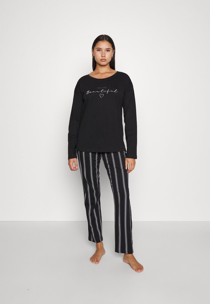 Haut à manches longues noir avec texte en script blanc et pantalon à rayures noir et blanc. Les deux articles sont en tissu doux et présentent une coupe décontractée.