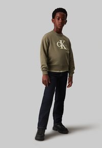 Felpa verde oliva con logo Calvin Klein, abbinata a jeans blu scuro e scarpe nere. Tessuto testurizzato, polsini e vita a coste.