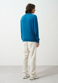 Pull turquoise en tissu doux avec un col rond, associé à un pantalon texturé ivoire et des baskets de couleur claire.