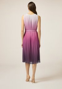 Rochie midi pliată cu un gradient de la roz deschis la violet închis, cu talie ajustată și decolteu rotund. Poartă tocuri nude.