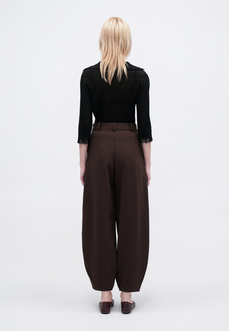 Pantaloni larghi marroni con vita alta, abbinati a un top nero a maniche tre quarti con texture, dotato di frange ai polsini.