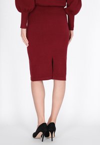 Fustă conică tricotată burgundy, cu o fanta la spate, asortată cu tocuri înalte din suede negru. Țesătura este netedă, cu un finisaj texturat.
