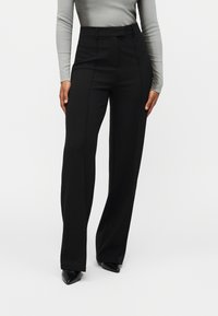 Μαύρο παντελόνι με υψηλή μέση, σχέδιο με ίσια πόδια και διακριτικές πιέτες στο μπροστινό μέρος. Το ύφασμα έχει λεία υφή και είναι ελαφρύ.