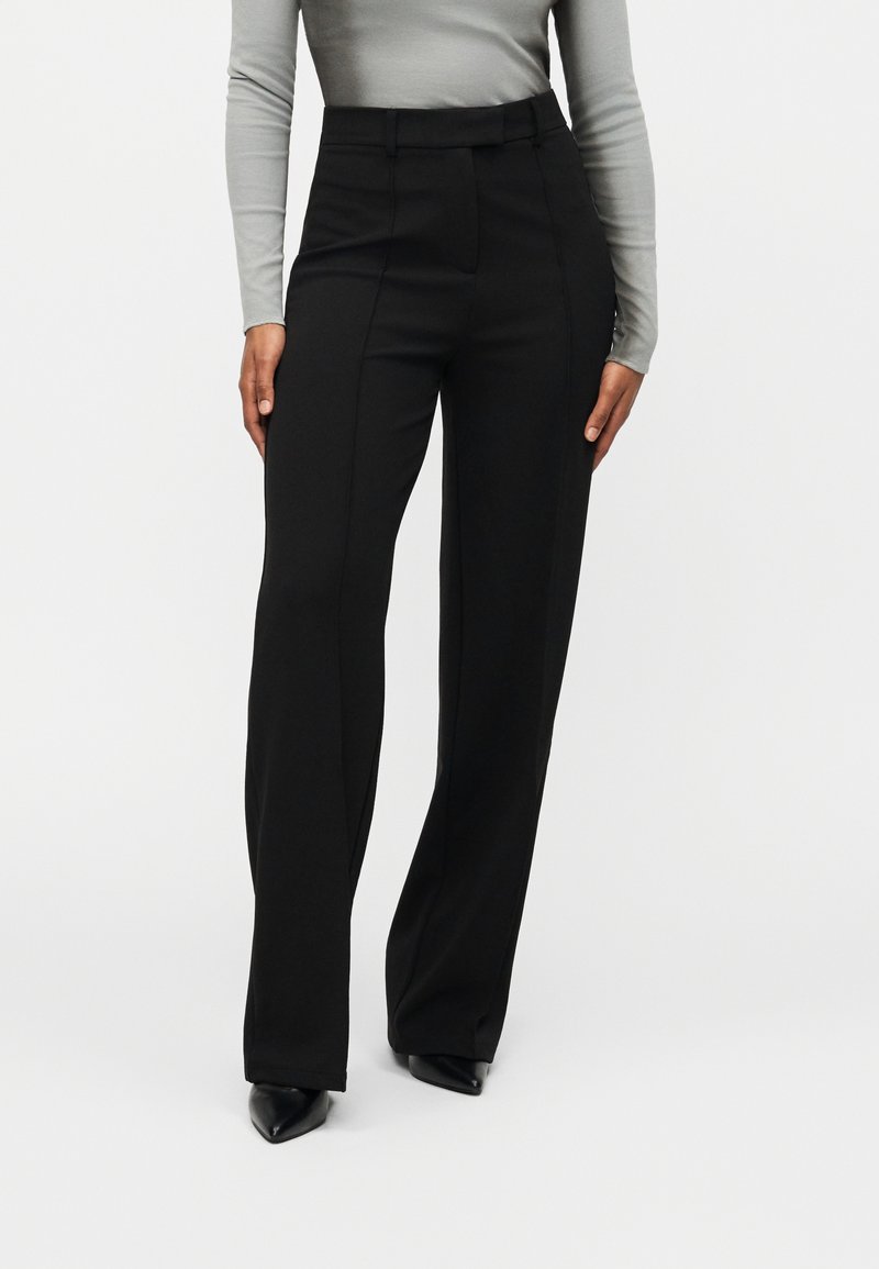 Μαύρο παντελόνι με υψηλή μέση, σχέδιο με ίσια πόδια και διακριτικές πιέτες στο μπροστινό μέρος. Το ύφασμα έχει λεία υφή και είναι ελαφρύ.