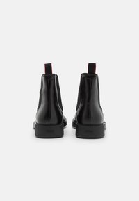 Bottes courtes en cuir noir avec panneaux élastiques latéraux, une finition lisse et un onglet de tirage décoratif rouge. Dotées d'une semelle en caoutchouc texturée.