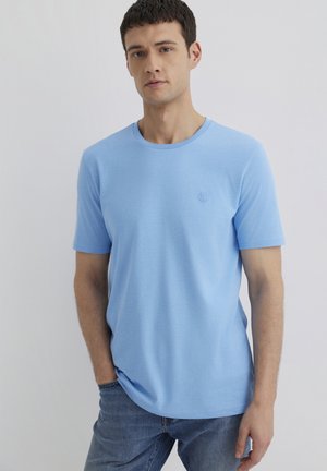 Helles blaues Baumwoll-T-Shirt mit kurzen Ärmeln, rundem Ausschnitt und dezentem, gesticktem Logo auf der Brust. Glatte Textur, lässige Passform.