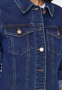 Mörkblå denimjacka med krage, böjda bruna knappar, två bröstfickor och synliga stygn. 