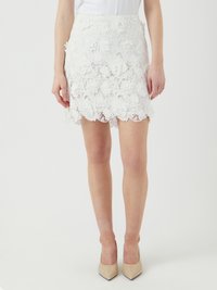 Mini-jupe blanche en dentelle avec des motifs floraux, un ourlet festonné, une doublure intérieure et une taille ajustée. Assortie à des talons pointus nude.