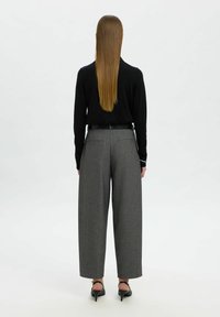 Maglietta nera a maniche lunghe abbinata a pantaloni grigi a gamba larga a vita alta. Il tessuto ha una sottile texture; scarpe con tacco completano il look.