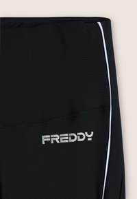 Leggings deportivos negros con piping blanco en los laterales. Presentan un logo "FREDDY" plateado brillante en la parte delantera, confeccionados con un tejido elástico y texturizado.