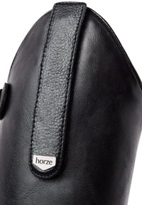 Bota de cuero negra con un acabado suave, puntera afilada y una correa negra texturizada con el logo "horze" en plata.