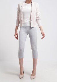 Lichtroze blazer over een wit top met textuur van kant, gecombineerd met grijze cropped leggings en nude hoge hakken. Gladde stof, getailleerde pasvorm.